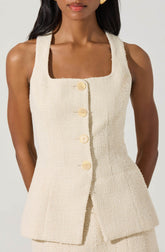 A woman wearing a sleeveless, cream-colored, textured fabric dress with a square neckline. The dress features a button-down front with large, round, cream-colored buttons and a fitted silhouette.